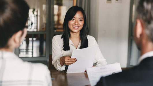 Business, career and recruitment concept - young asian woman smiling and holding resume while interviewing as candidate for job in big company